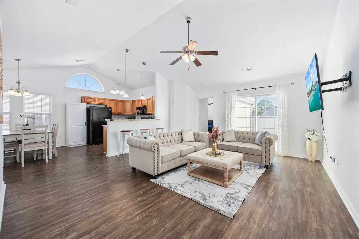 Open-plan living room with white sofas and a kitchen behind it